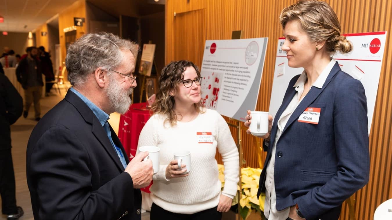 Three attendees stand around holding drinks by event materials